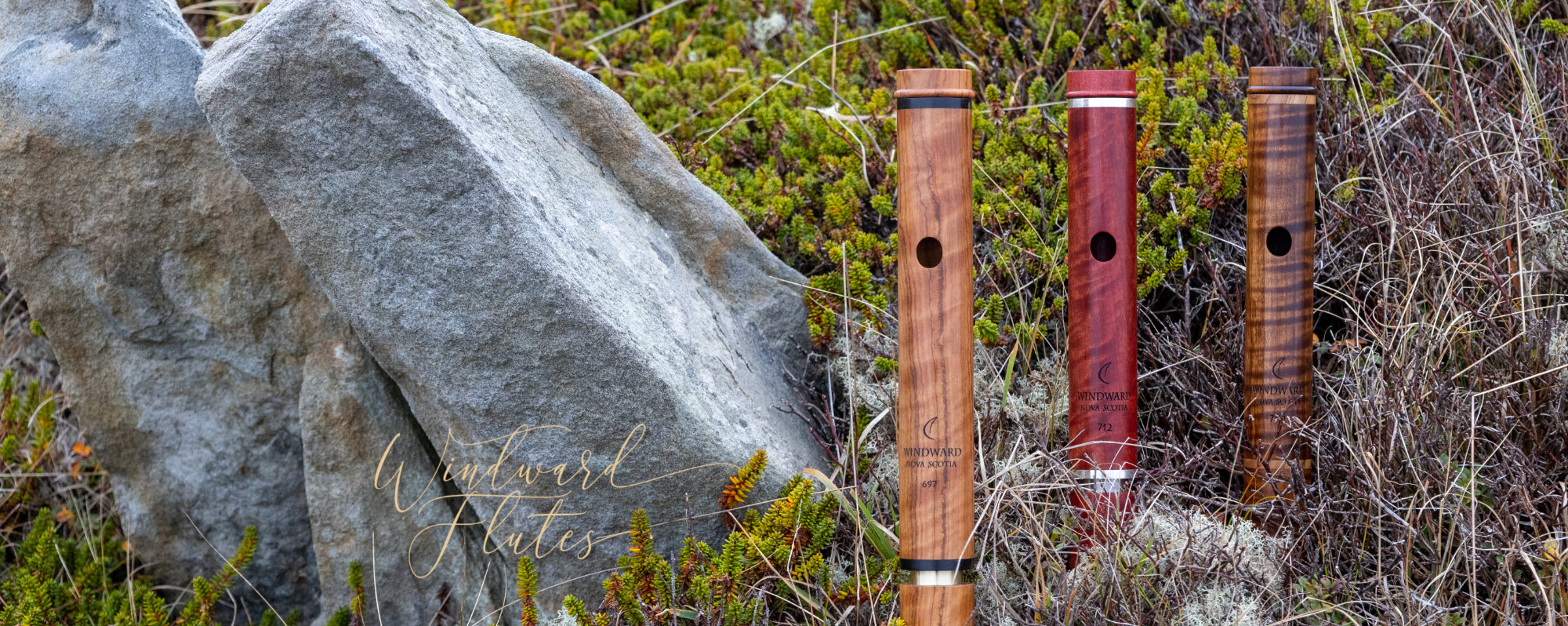 Three headjoints in front of rocks and lichen - in order from left to right - African Olive, Pink Ivory, and Thermally Treated maple.